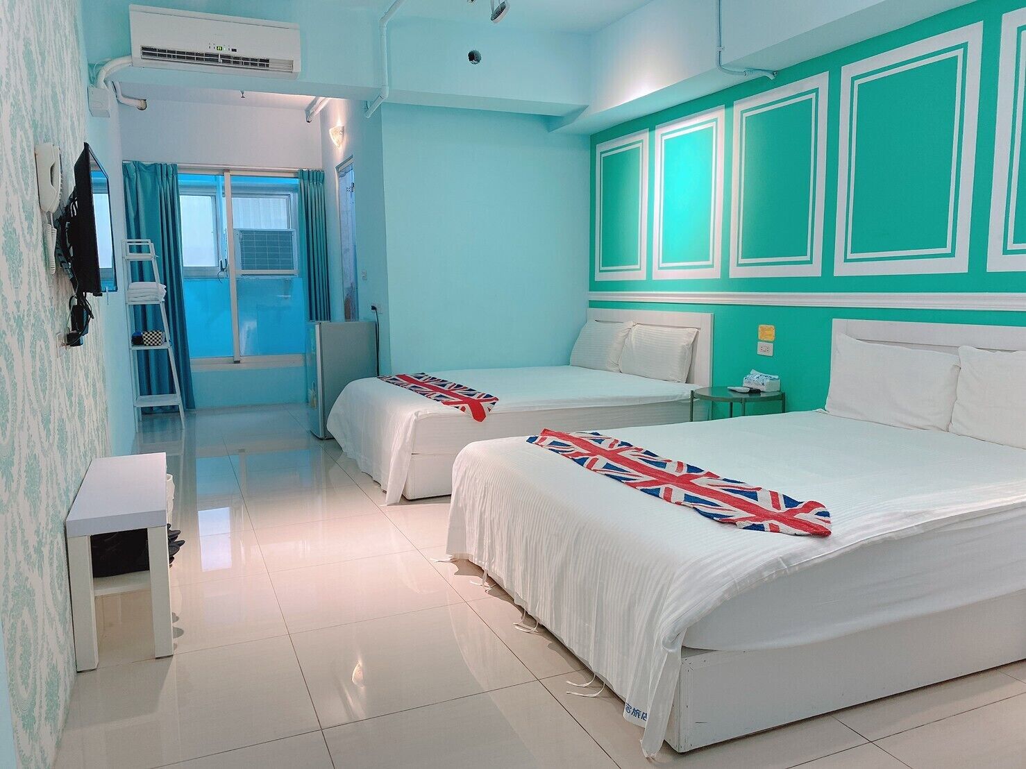A hotel room with two beds, a small table, a wardrobe, and a bathroom with a shower and toilet.