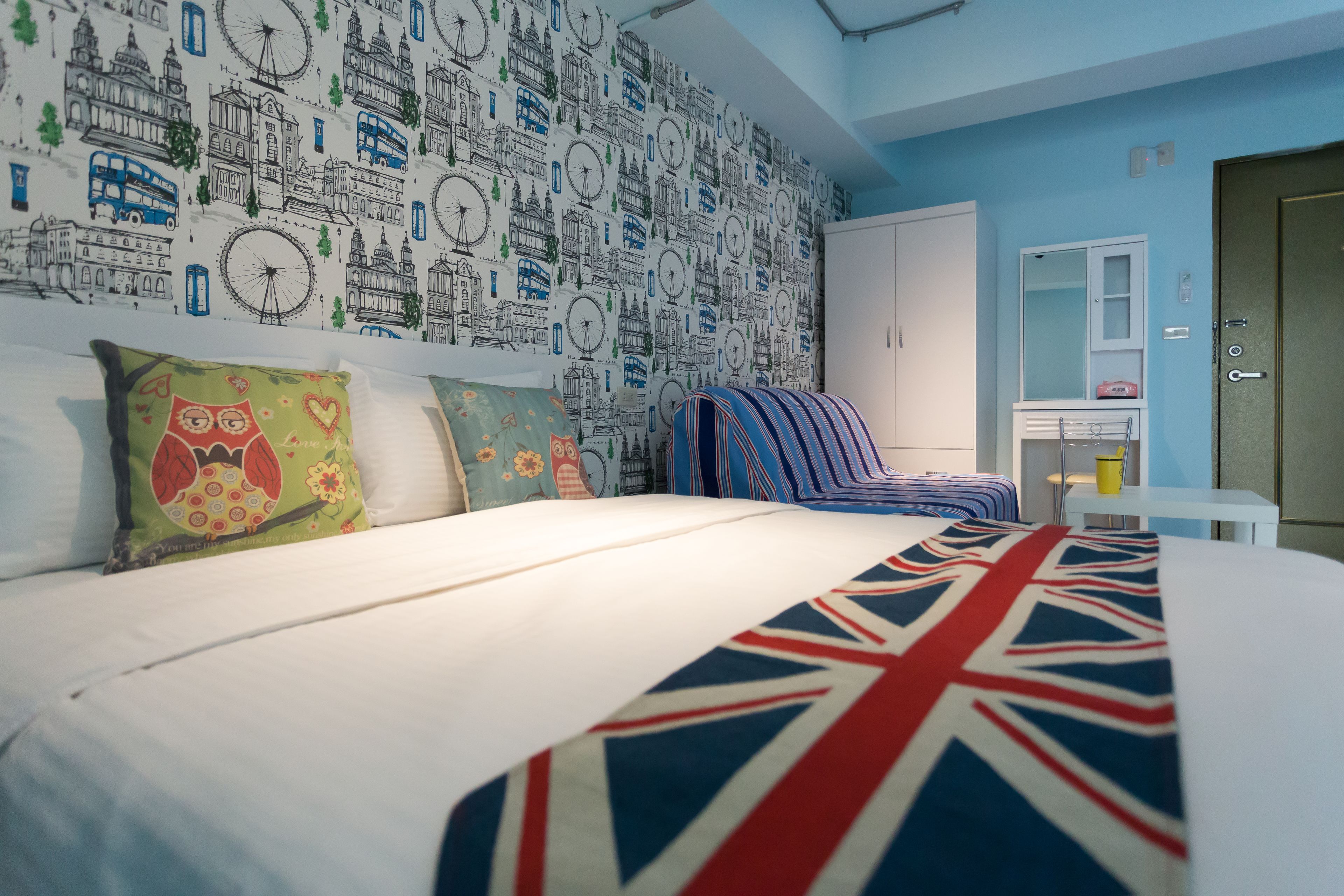 A hotel room with a large bed, a patterned wall, a small table, and a wardrobe.