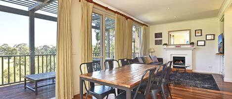 Una habitación amplia con una mesa de madera, sillas, una chimenea y un balcón con cortinas.