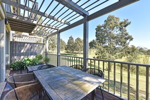 A covered outdoor patio with a wooden table and chairs, surrounded by a metal railing.