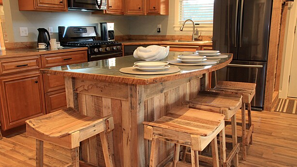 A kitchen with wooden bar stools, a central island, and stainless steel appliances. - The Red Hen Cottage-Asheville-with Hot Tub and EV charger! (Asheville)