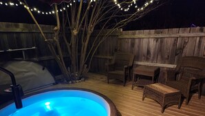 A hot tub with a wooden deck, surrounded by wicker chairs and a wooden fence. - The Red Hen Cottage-Asheville-with Hot Tub and EV charger! (Asheville)
