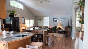 A spacious kitchen with a large island, wooden bar stools, and a dining area with a sofa and table. - The Red Hen Cottage-Asheville-with Hot Tub and EV charger! (Asheville)