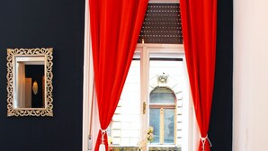 Ein Essbereich mit einem Holztisch, weißen Stühlen, roten Vorhängen und einem Spiegel an der Wand.
