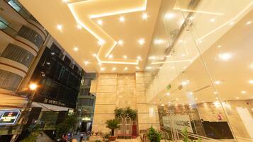 Un moderno hall de hotel con un diseño de iluminación geométrico en el techo, una recepción y vistas a la calle.