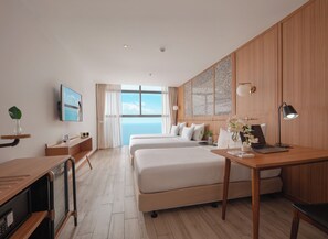 Une chambre d’hôtel avec deux lits, un bureau, une télévision et une vue sur la mer.