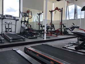 Een sportschool met diverse fitnessapparaten, waaronder loopbanden, krachttrainingsmachines en losse gewichten.