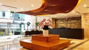 Zona de recepción de hotel con diseño moderno, que cuenta con un mostrador de madera, un jarrón grande con orquídeas rosas y una pared con el letrero 'Majestic Premium'.