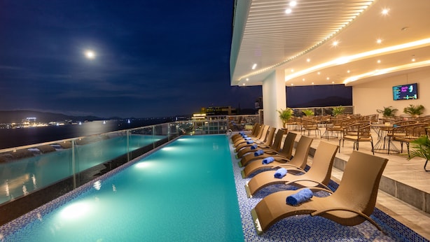 Zona junto a la piscina con sillones de descanso y vista al mar de noche.
