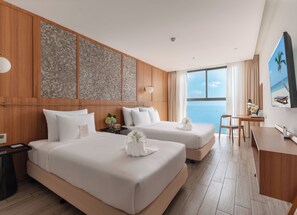 Une chambre d’hôtel avec deux lits, un bureau, une télévision et une grande fenêtre donnant sur la mer.
