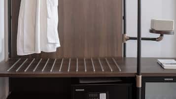 Habitación de hotel con un armario de madera oscura, estructura de cama metálica negra, bata blanca colgada en el armario, microondas y una pequeña mesa con un libro.