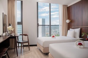 Une chambre d’hôtel équipée d’un bureau, de deux lits, d’une chaise, d’une fenêtre donnant sur des immeubles et d’une lampe fixée au mur.