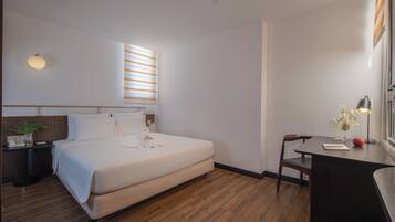 Una habitación de hotel con cama, mesita de noche, escritorio, silla y ventana con persianas.