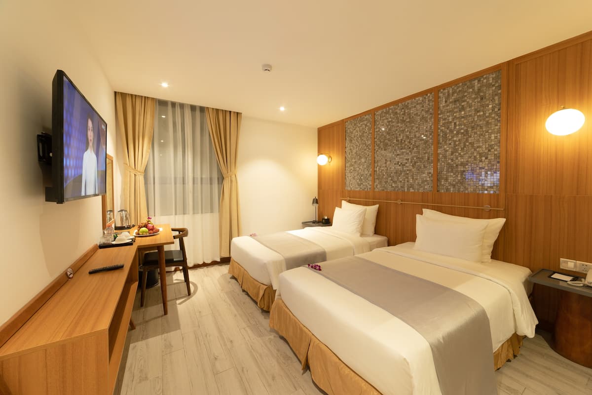 A hotel room with two beds, a desk with a television, and a dining area.