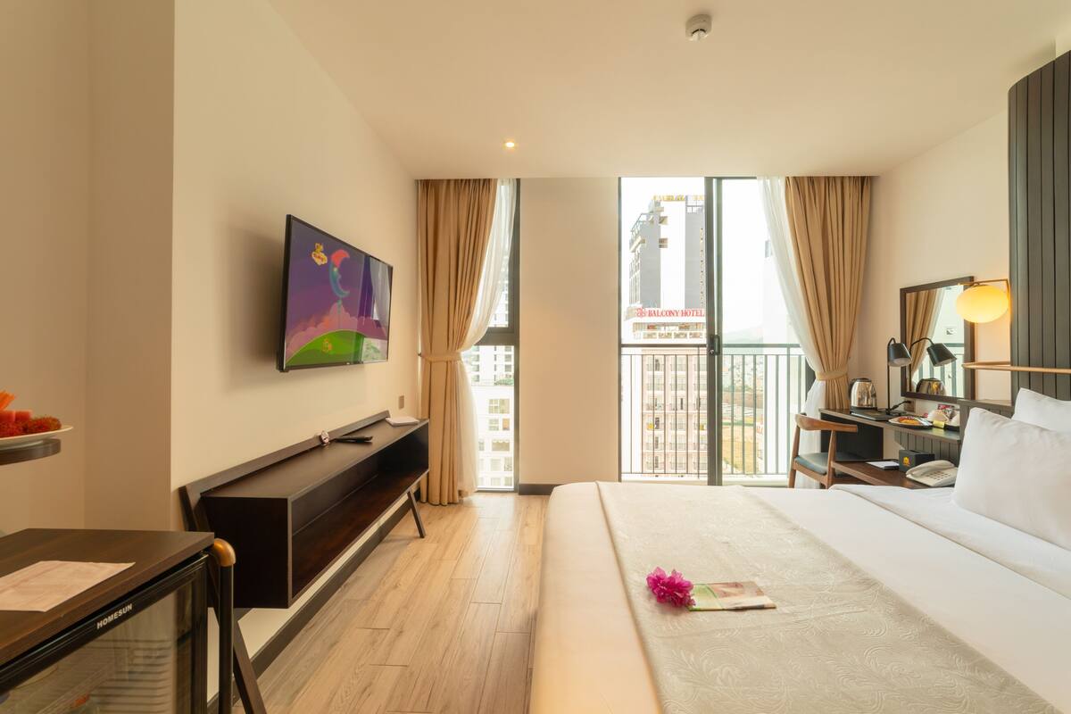 A hotel room with a bed, a desk, a TV, and a balcony with curtains.