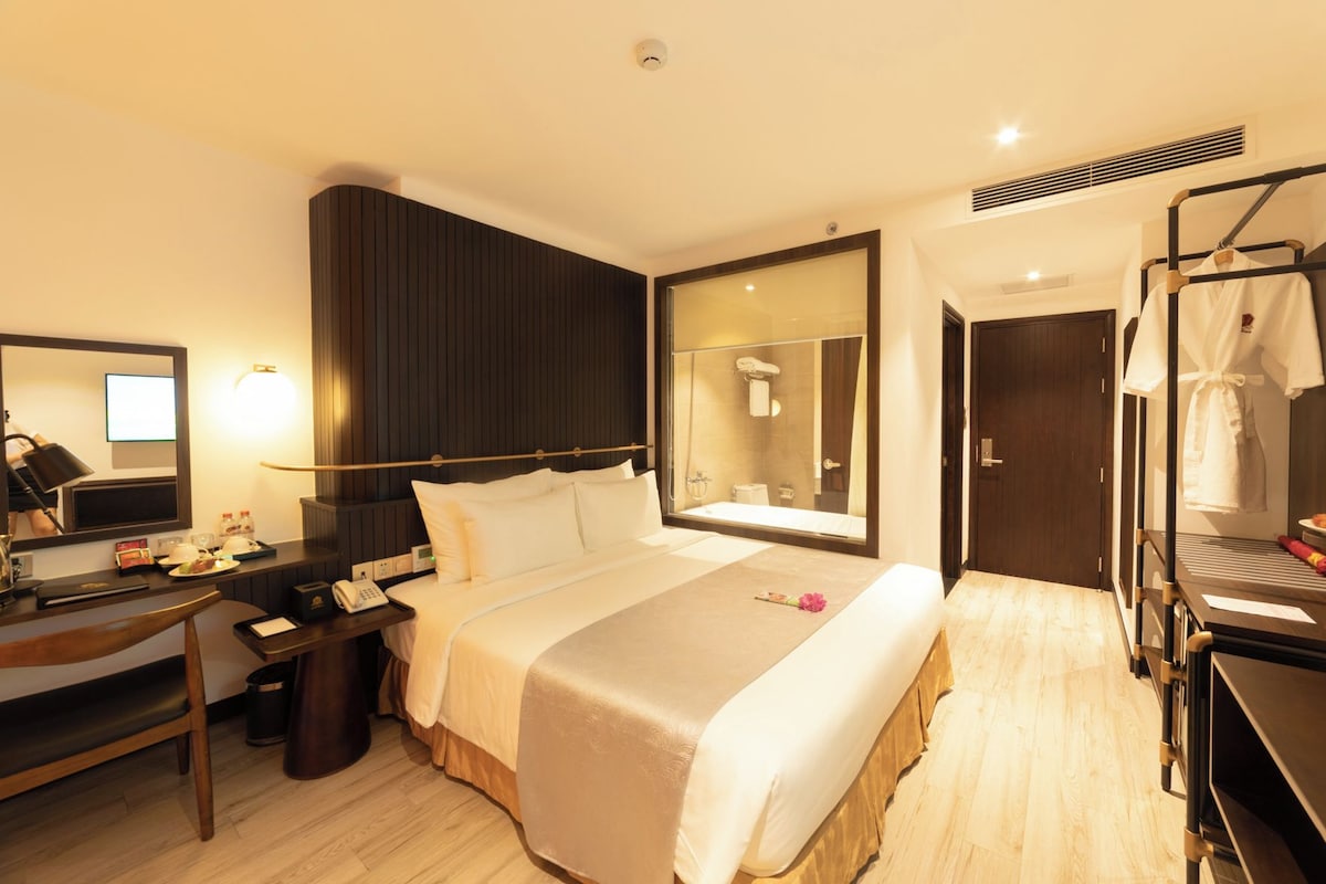 Une chambre d’hôtel comprenant un lit, un bureau avec un téléphone, un miroir, une armoire et une salle de bain visible à travers une porte en verre.