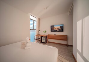 Ett hotellrum med en säng, ett skrivbord, ett litet kylskåp, ett fönster med utsikt över havet och en tavla på väggen.