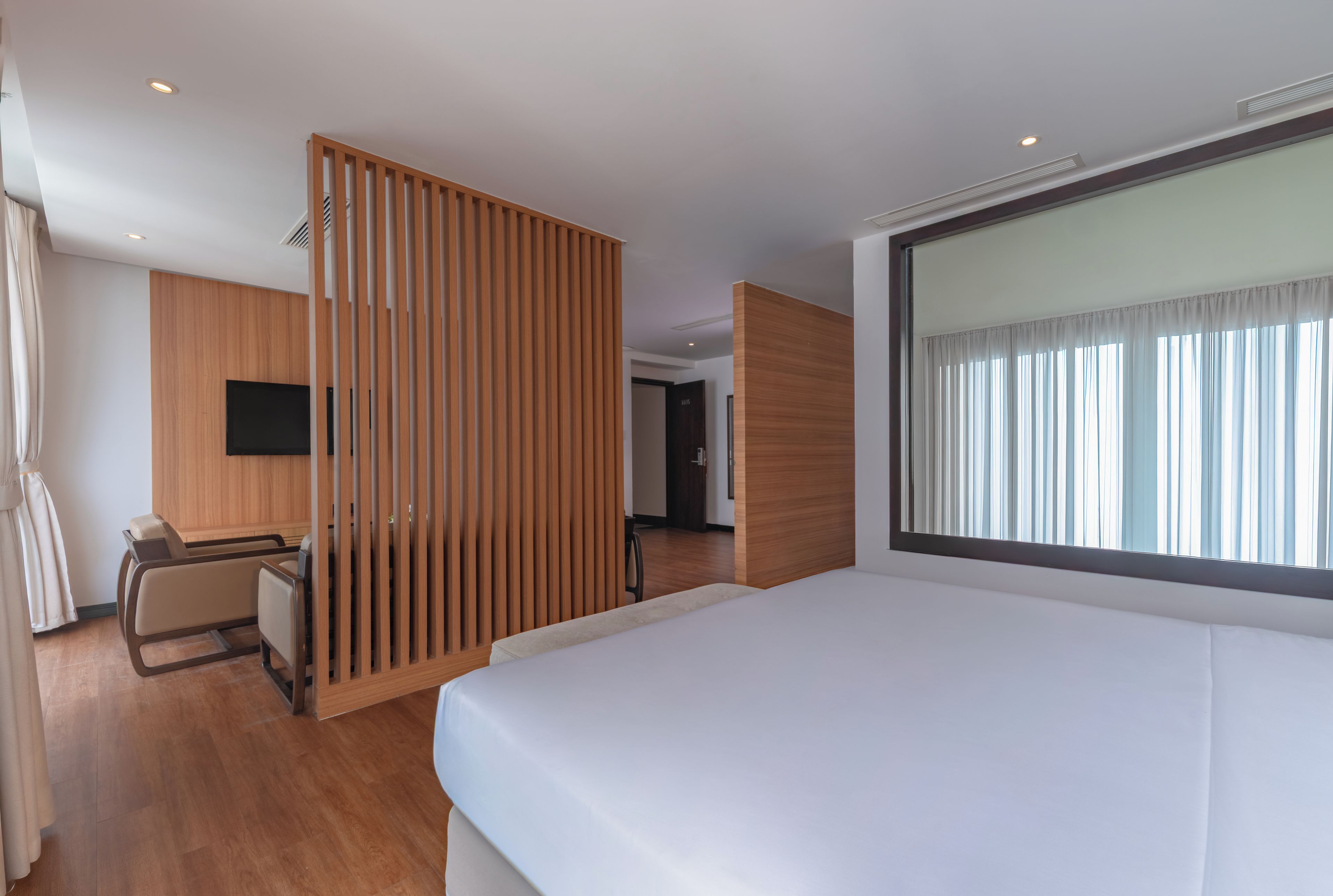 A hotel room with a bed, a desk, a chair, a TV, and a large window with curtains.
