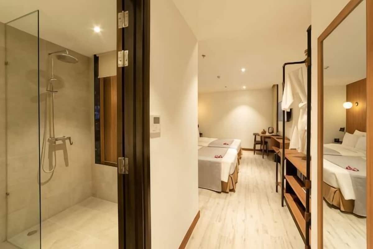 Ein Hotelzimmer mit Glasdusche, einem Bett mit Holz-Kopfteil, einem Nachttisch und einem Spiegel.