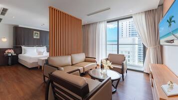 A hotel room with a bed, sofa, chairs, a coffee table, and a view of the beach.