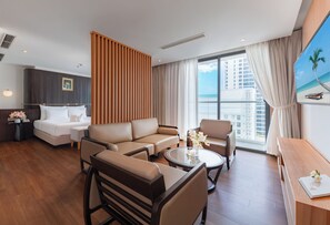 Habitación de hotel con cama, sofá, sillas, una mesa de centro y vista a la playa.