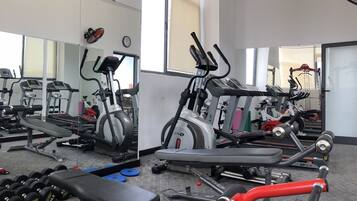 Un gimnasio con varios equipos de ejercicio, incluyendo cintas de correr, elípticas y pesas sueltas.