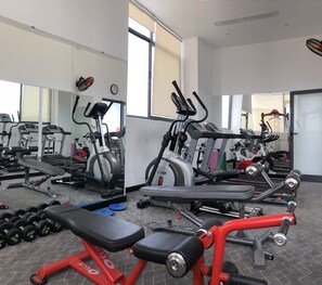 Een sportschool met diverse fitnessapparaten, waaronder loopbanden, crosstrainers en losse gewichten.