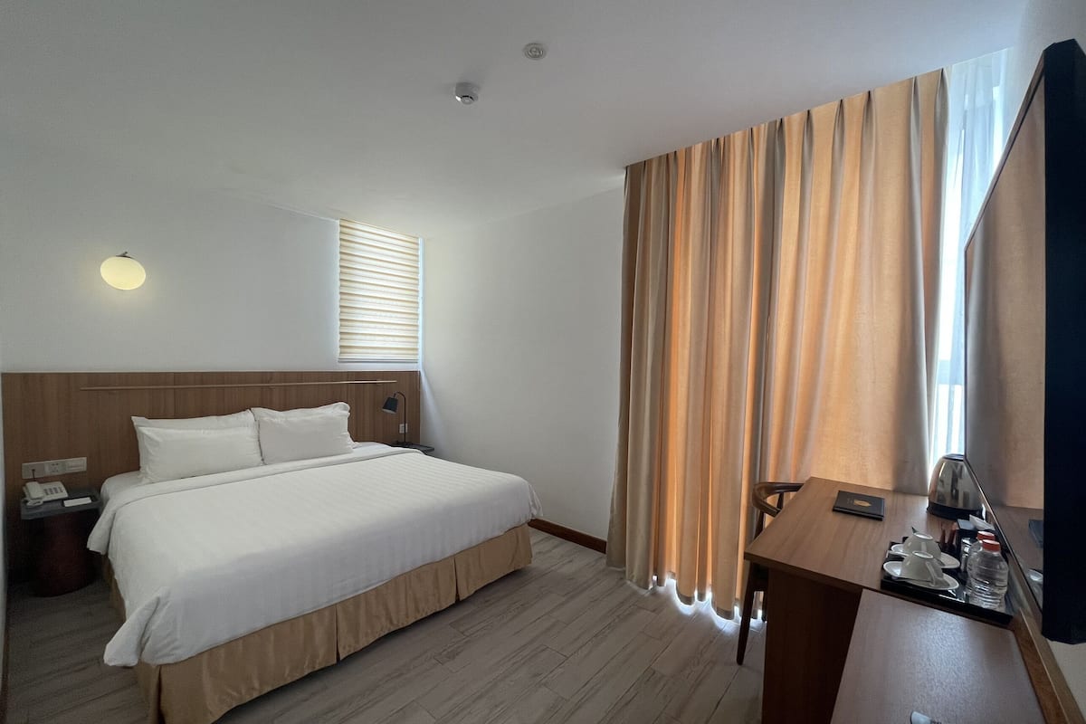 A hotel room with a large bed, a desk with a chair, a telephone, and a flat-screen TV.