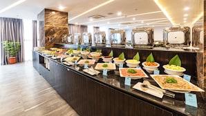 Buffet com diversos alimentos e parede de mármore ao fundo.