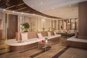 A modern lobby with a curved wooden reception desk, seating areas, and a glass coffee table.