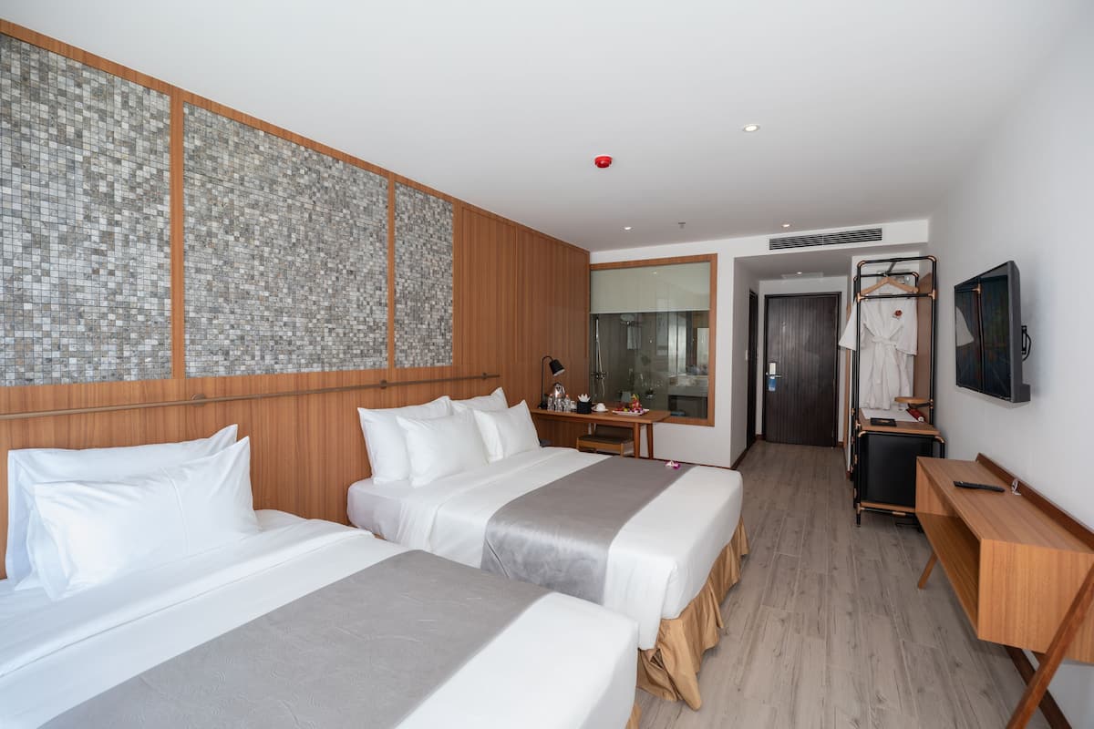 A hotel room with two beds, a wooden headboard, a large mirror, a desk, and a TV.