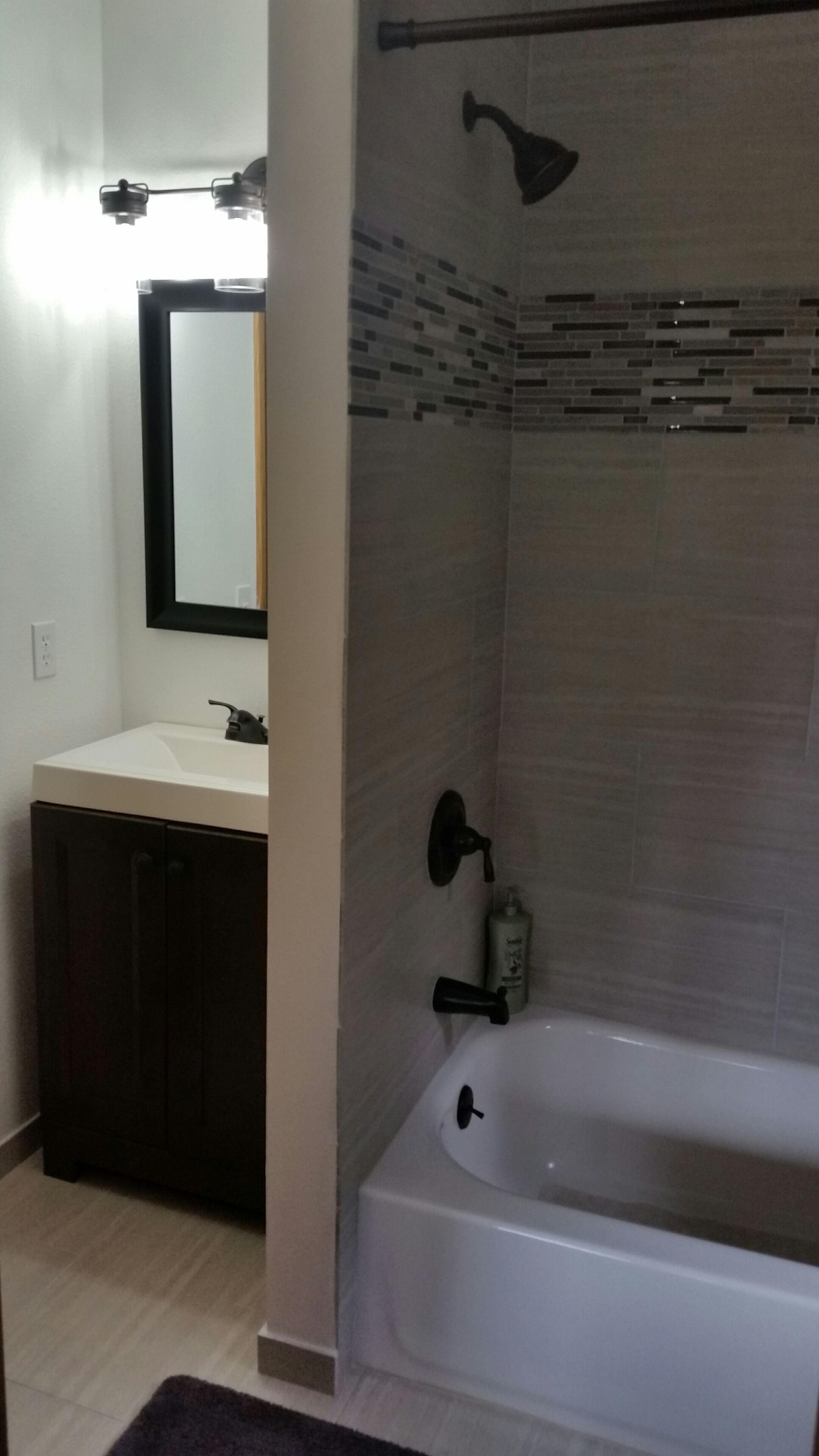 A bathroom with a white bathtub, a showerhead, and a sink with a mirror above it.