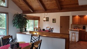 Une cuisine avec des meubles en bois, un coin repas avec une table et des chaises, et une grande fenêtre donnant sur des arbres.