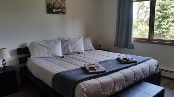 A neatly made bed with a grey and white duvet, pillows, and a folded towel on the bed.
