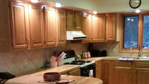 Une cuisine avec des meubles de rangement en bois, une cuisinière à gaz, un évier et une horloge au mur.