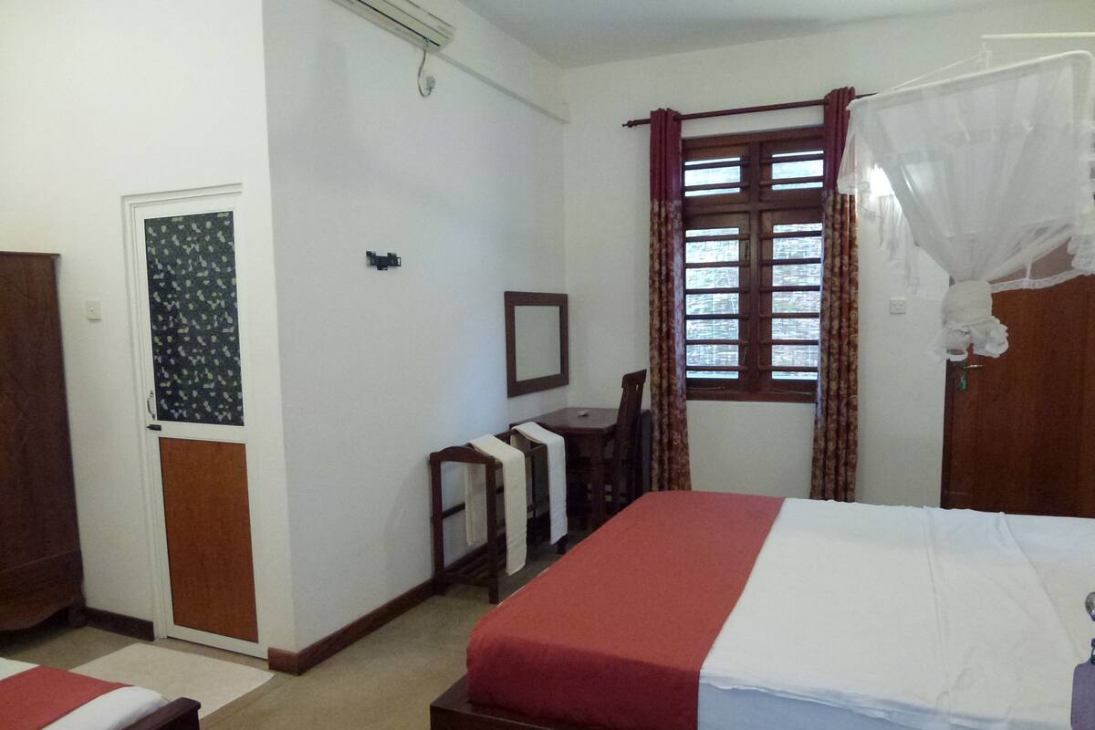 Une chambre d’hôtel avec un lit, un bureau, une chaise, une armoire et une fenêtre avec des rideaux.