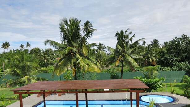 A pool area with wooden lounge chairs and a covered seating area, surrounded by palm trees and greenery. - Weligama Ocean Breeze (Weligama)