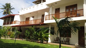 A two-story building with balconies, a covered patio, and a well-maintained garden with palm trees and shrubs. - Weligama Ocean Breeze (Weligama)