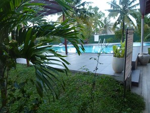 A pool area with a tiled deck, surrounded by lush greenery and palm trees. - Weligama Ocean Breeze (Weligama)