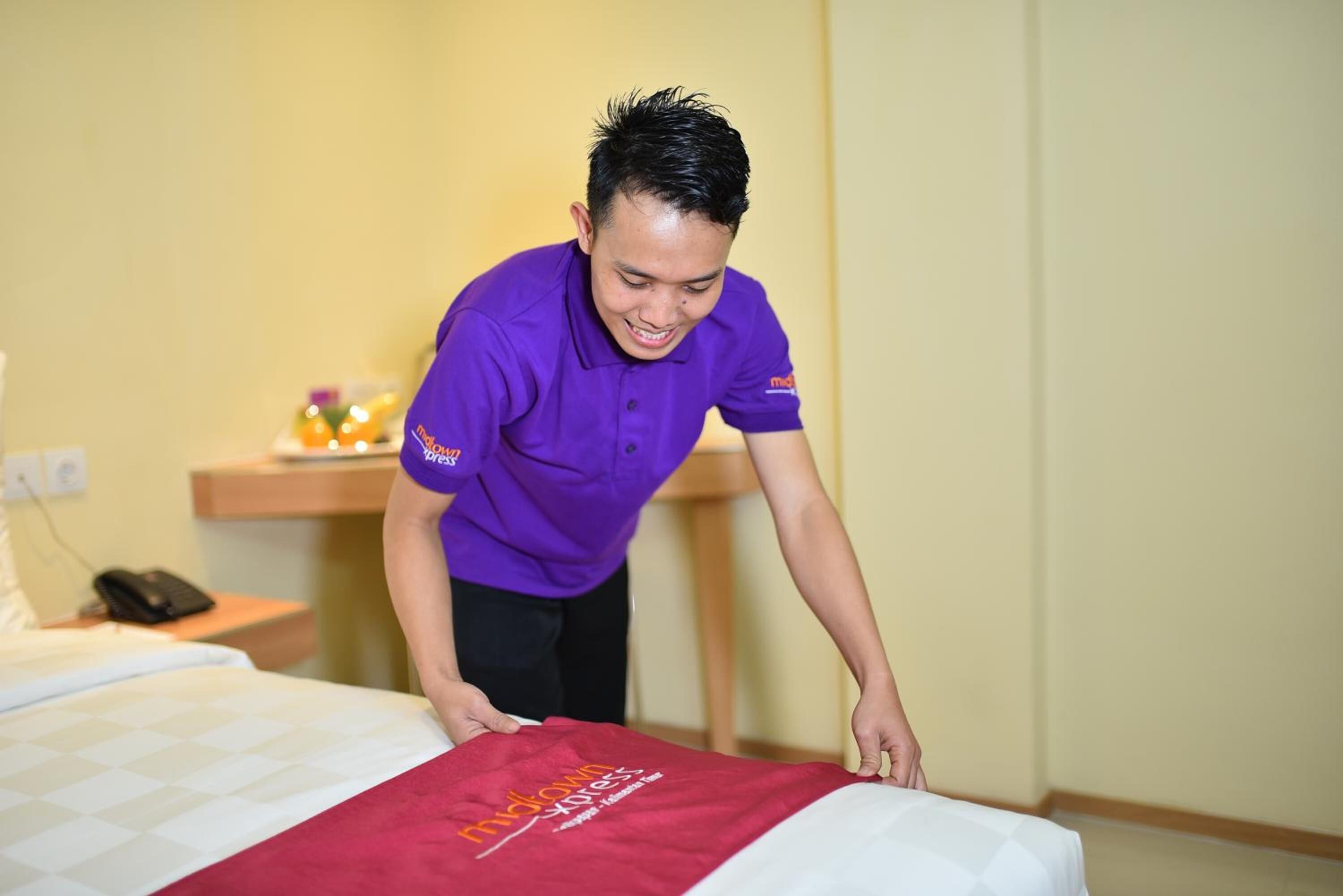 A person in a purple uniform adjusting a bed with a red blanket in a hotel room.