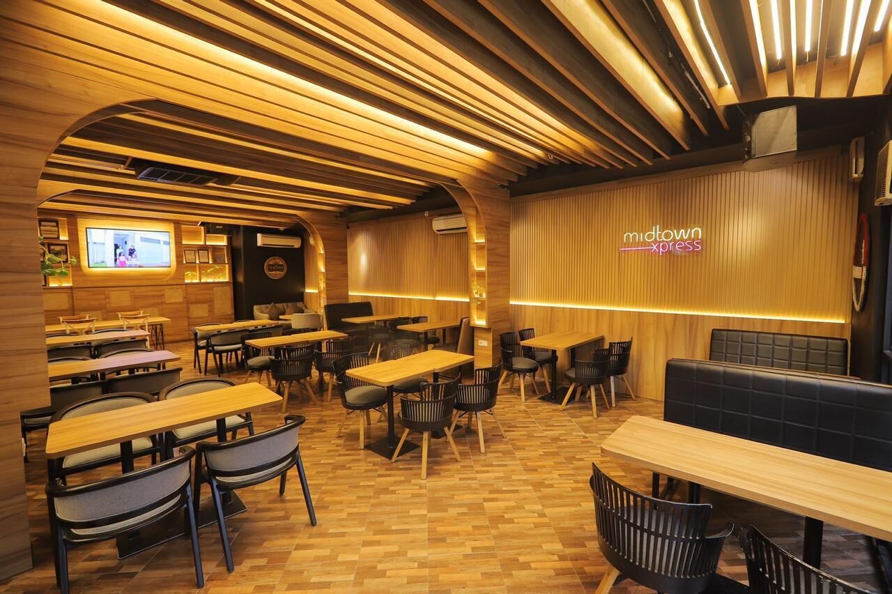 A modern restaurant interior with wooden tables and chairs, a neon sign, and a TV screen.