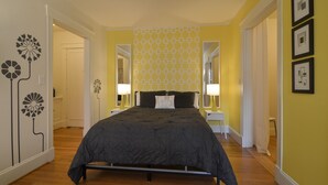 Un dormitorio con cama, mesita de noche, lámpara y pared con diseño geométrico.