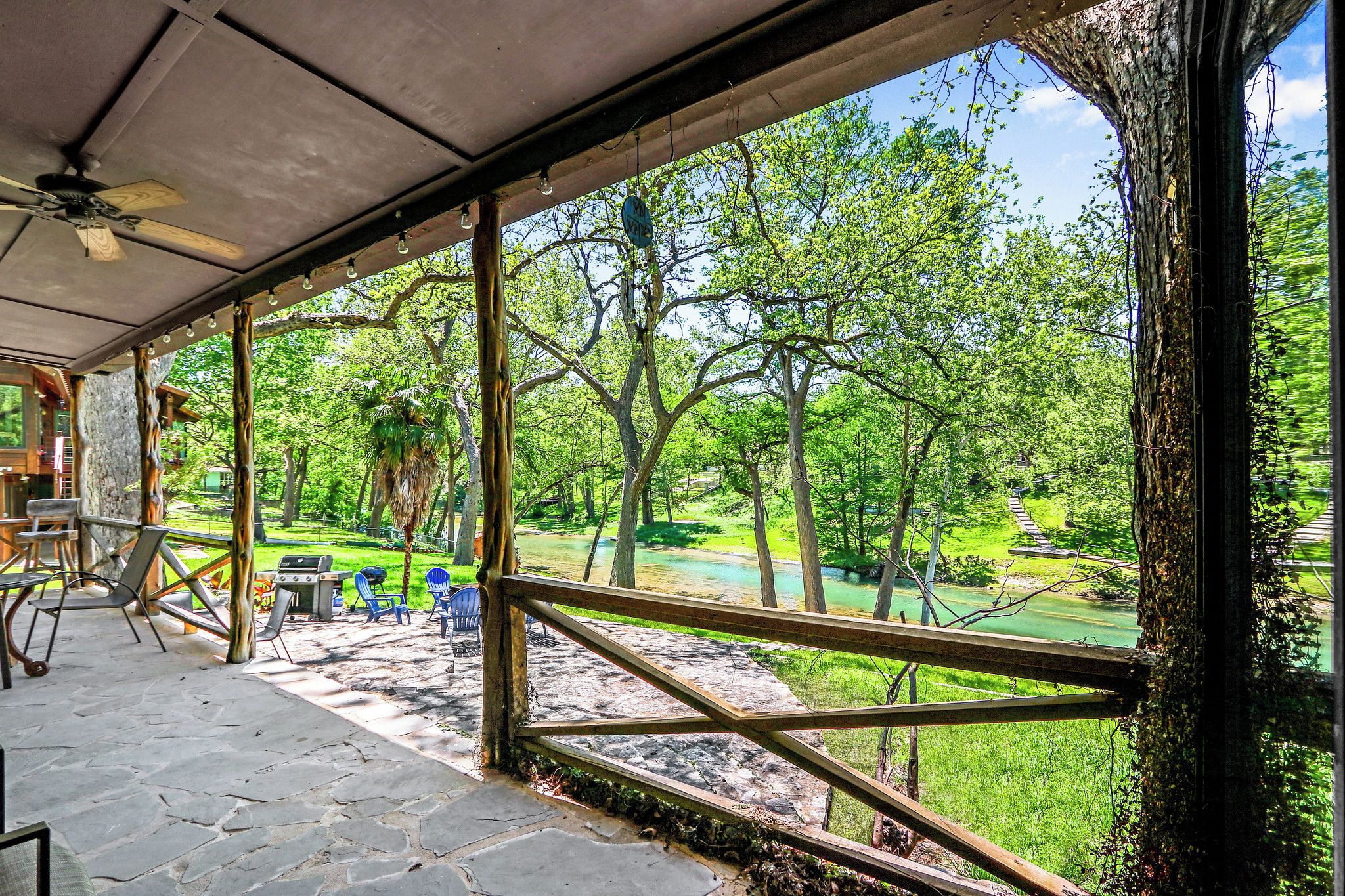 Une terrasse couverte avec des sièges d’extérieur, une vue sur un paysage verdoyant et une clôture en bois.
