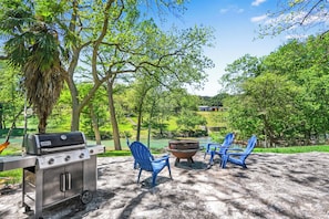 An outdoor barbecue area with a grill, two Adirondack chairs, and a fire pit. - The Guadalupe River right in your backyard! River living at its best! (New Braunfels)