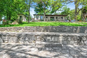 A stone wall with a grassy area and a building with a porch and outdoor seating. - The Guadalupe River right in your backyard! River living at its best! (New Braunfels)