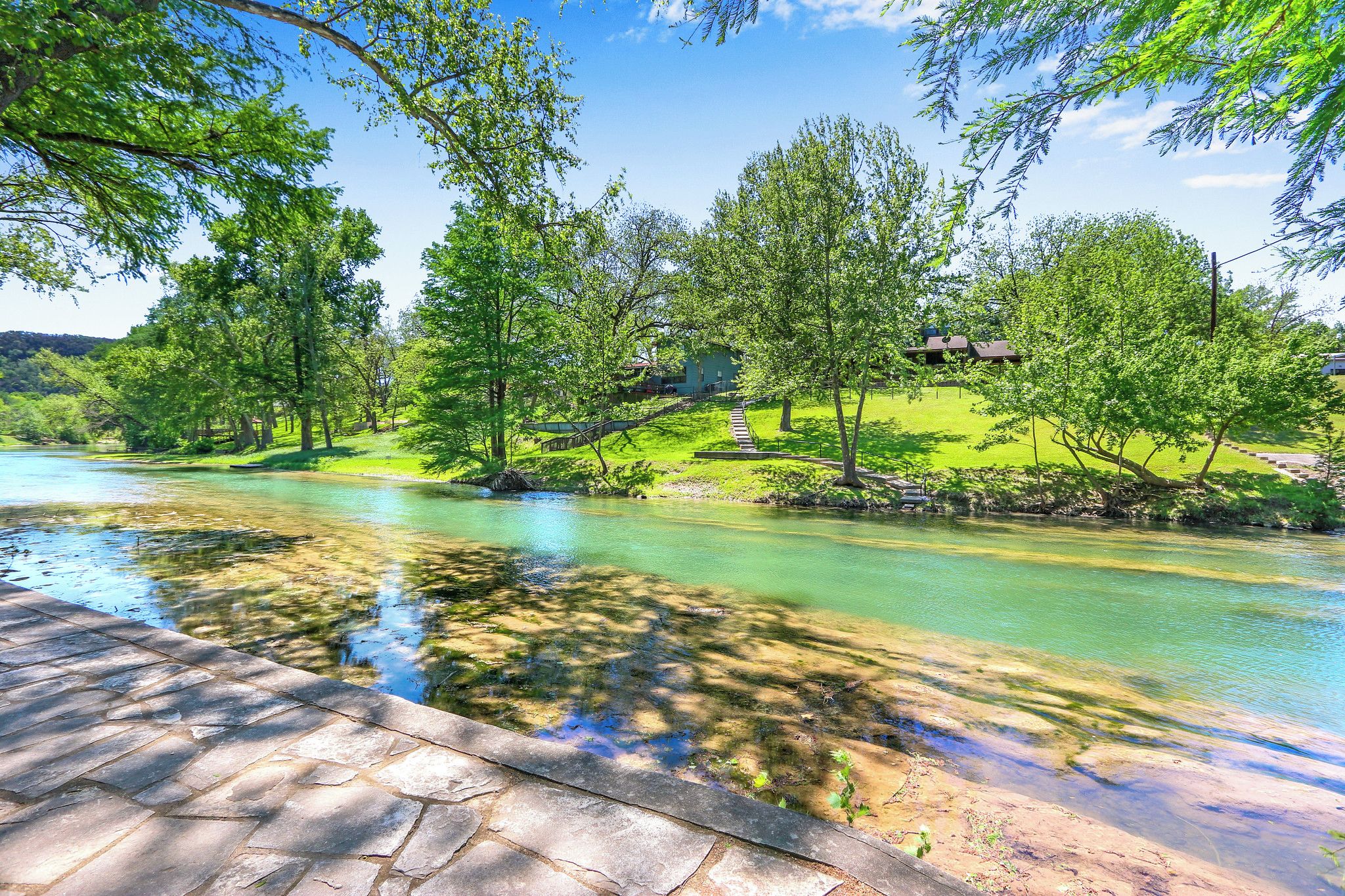 A river with clear water, surrounded by lush green trees and a stone pathway.