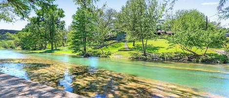 A river with clear water, surrounded by lush green trees and a stone pathway.