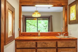 Un tocador de madera con espejo, lavabo e iluminación colgante.