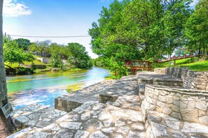 A stone pathway leading to a river with a 'No Parking' sign, surrounded by lush greenery and a clear sky. - The Guadalupe River right in your backyard! River living at its best! (New Braunfels)