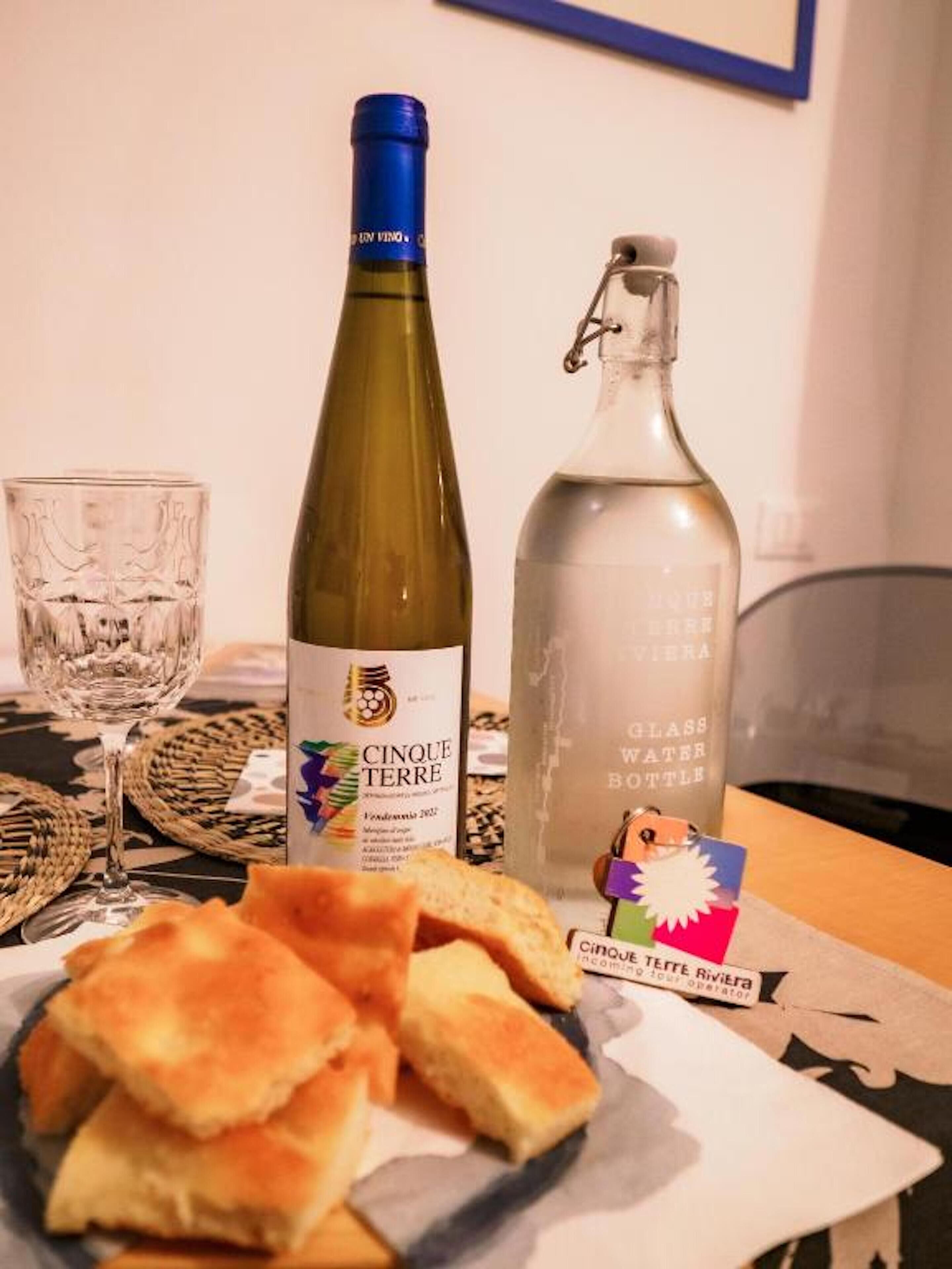 Una mesa con una botella de vino, una copa y un plato de pan.